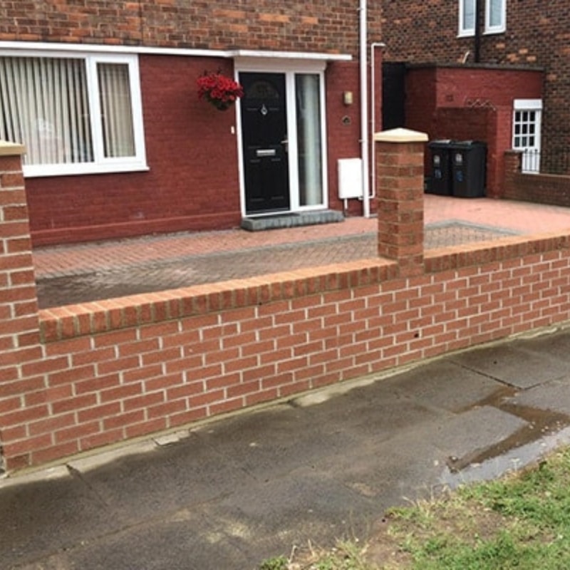 A brick wall featuring a gate and a fence, creating a defined boundary in an outdoor setting.